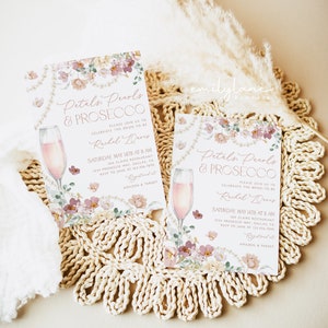 May include: Two pink and white floral bridal shower invitations with a glass of prosecco on each. The text on the invitations reads "Petals, Pearls & Prosecco" and "Please join us to celebrate the bride-to-be Rachel Davis".