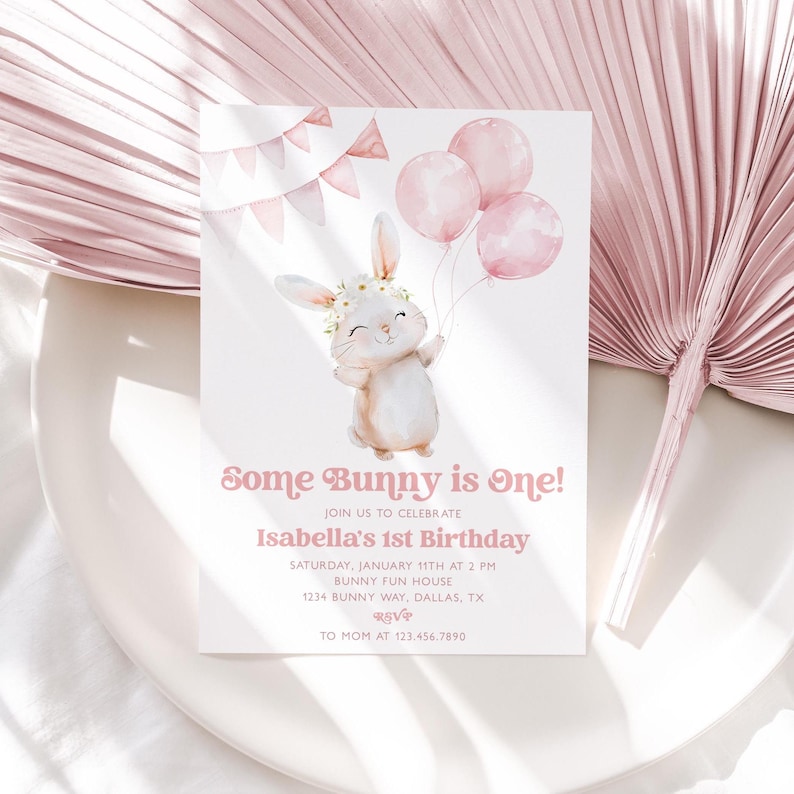 Op de afbeelding: Een roze en witte uitnodigingskaart met een aquarel-illustratie van een konijn dat ballonnen vasthoudt. De tekst op de kaart luidt "Some Bunny is One!" en "Isabella's 1st Birthday".