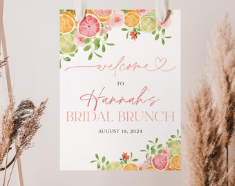 Może przedstawiać: Biały znak z akwarelowym wzorem różowych kwiatów i owoców cytrusowych. Tekst na znaku brzmi: "Witamy na brunch'u ślubnym Hanny 19 sierpnia 2024".