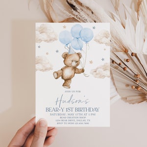 May include: A blue and brown birthday invitation with a cartoon bear holding blue balloons and a party hat. The invitation says "Join us for Hudson's Bear-Y 1st Birthday" with the date, time, location, and RSVP information.