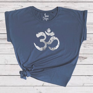 以下が含まれることがあります： 紺色のTシャツに、シルバーのオームのシンボルが前面にプリントされています。シンボルは、使い古したヴィンテージな外観をしています。Tシャツは、袖をまくり上げて、ゆったりとしたフィット感です。