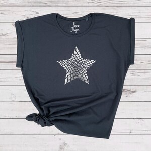 Pu&ograve; includere: Una maglietta grigia scura con una stampa a stella argentata. La stella ha un motivo a pelle di serpente. La maglietta ha una vestibilit&agrave; rilassata e maniche arrotolate. Inca Designs &egrave; stampato sul davanti della maglietta.