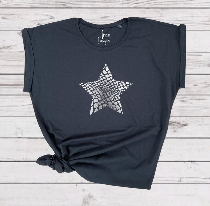 Pu&ograve; includere: Una maglietta grigia scura con una stampa a stella argentata. La stella ha un motivo a pelle di serpente. La maglietta ha una vestibilit&agrave; rilassata e maniche arrotolate. Inca Designs &egrave; stampato sul davanti della maglietta.