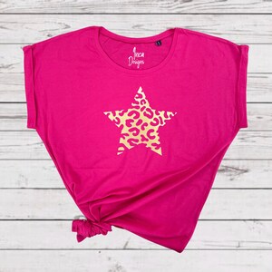 Pu&ograve; includere: Una maglietta rosa brillante con una stella dorata con un motivo a stampa leopardata. La maglietta ha una vestibilit&agrave; rilassata e un orlo annodato. Il testo "Inca Designs" &egrave; stampato sul davanti della maglietta.