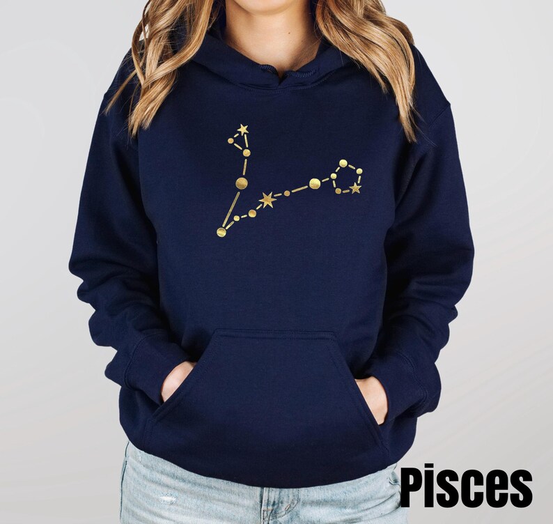 May include: A navy blue hoodie with a gold Pisces constellation design. The hoodie has a drawstring hood and a kangaroo pocket.