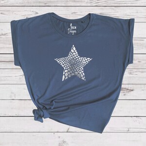 Pu&ograve; includere: Una t-shirt blu navy con una stampa a stella argentata. La stella ha un motivo a pelle di serpente. La t-shirt ha una manica arrotolata e il testo "Inca Designs" &egrave; stampato sul davanti.