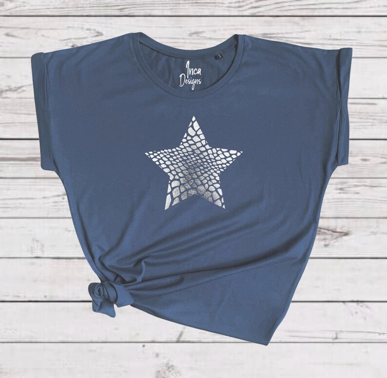 Pu&ograve; includere: Una t-shirt blu navy con una stampa a stella argentata. La stella ha un motivo a pelle di serpente. La t-shirt ha una manica arrotolata e il testo "Inca Designs" &egrave; stampato sul davanti.