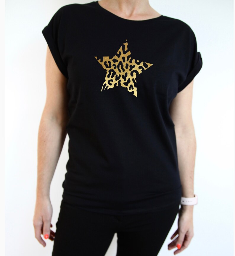 Pu&ograve; includere: Maglietta nera con una stampa a stella dorata con un design a stampa leopardata.