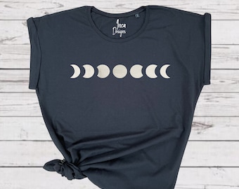 May include: A black t-shirt with a silver moon phase design. The shirt has a relaxed fit and rolled up sleeves. The text "Inca Designs" is printed on the shirt.