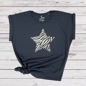 Pu&ograve; includere: Maglietta nera con una grande stella dorata stampata sul davanti. La stella ha un motivo a zebrato. La maglietta ha una manica arrotolata e dice "Inca Designs" sul davanti.