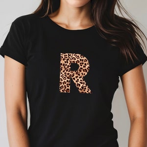 May include: Black t-shirt with a large letter "R" printed on the front. The letter is made of a leopard print pattern in shades of brown and tan.