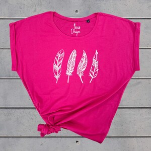 Może przedstawiać: Jasnor&oacute;żowy t-shirt z białym nadrukiem pięciu stylizowanych pi&oacute;r. Na przodzie koszulki widnieje napis "Inca Designs".