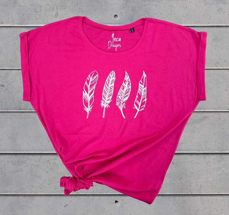 Może przedstawiać: Jasnor&oacute;żowy t-shirt z białym nadrukiem pięciu stylizowanych pi&oacute;r. Na przodzie koszulki widnieje napis "Inca Designs".