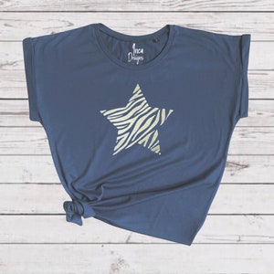 Pu&ograve; includere: Una t-shirt blu navy con un design a stella con stampa zebrata bianca e dorata. La t-shirt ha una vestibilit&agrave; rilassata e maniche arrotolate. Il testo "Inca Designs" &egrave; stampato sulla t-shirt.