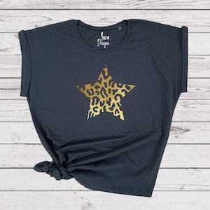 Pu&ograve; includere: Maglietta nera con una stella dorata stampata sul davanti. La stella &egrave; riempita con un motivo leopardato. Il testo "Inca Designs" &egrave; stampato sulla maglietta.