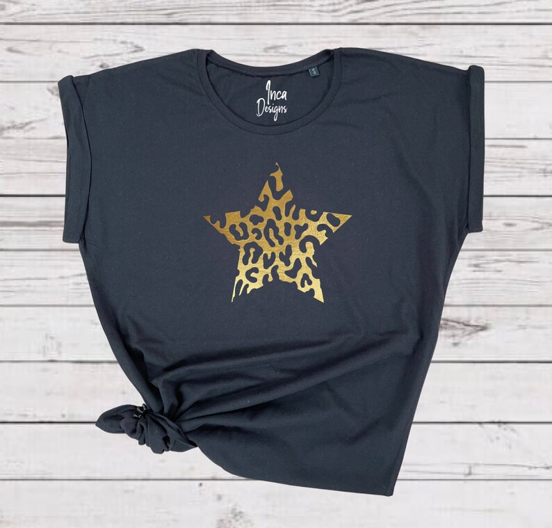 Pu&ograve; includere: Maglietta nera con una stella dorata stampata sul davanti. La stella &egrave; riempita con un motivo leopardato. Il testo "Inca Designs" &egrave; stampato sulla maglietta.