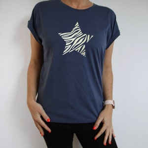 Pu&ograve; includere: Una t-shirt blu navy con un grande design a stella con stampa zebrata bianca e dorata.