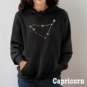 May include: Black hoodie with a gold Capricorn constellation design. The text "Capricorn" is printed below the design.