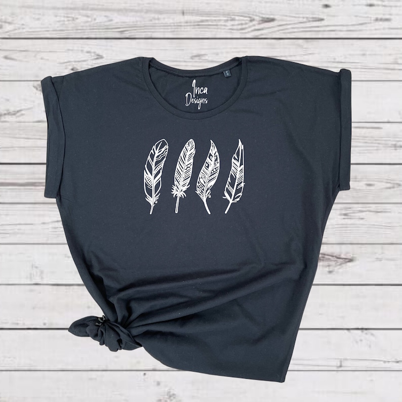 Może przedstawiać: Czarny T-shirt z białym wzorem czterech stylizowanych pi&oacute;r. Na koszulce nadrukowany jest tekst "Inca Designs".