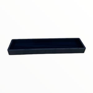 May include: A rectangular, black tray with a low profile. The tray is made of a solid material and has a smooth, matte finish. The interior of the tray is also black. The tray is empty and sits on a white surface.