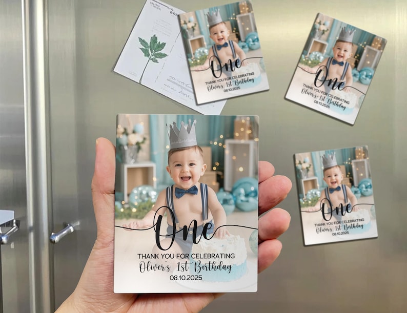 May include: Square magnets featuring a baby wearing a crown and bow tie, with the word "One" and the text "Thank You for Celebrating Oliver's 1st Birthday 08.10.2025". The magnets are light blue and white.