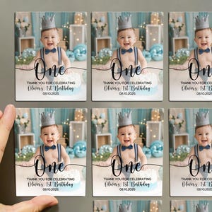 May include: Rectangular magnets featuring a baby wearing a crown and suspenders, with the word "One" in elegant script. The text reads "Thank you for celebrating Oliver's 1st Birthday 08.10.2025".