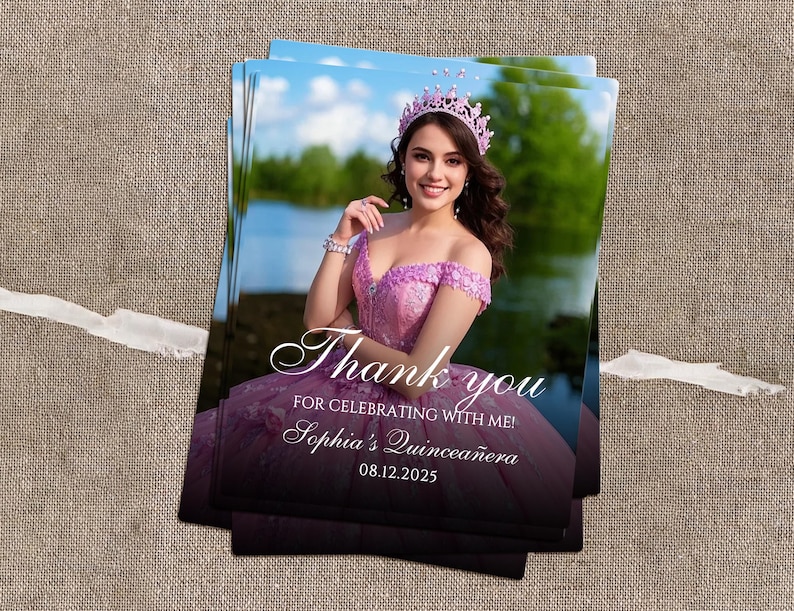 May include: A stack of printed cards featuring a woman in a pink dress and crown. The cards have the text "Thank you for celebrating with me! Sophia's Quincea&ntilde;era 08.12.2025" in a script font. The background shows a lake and trees.