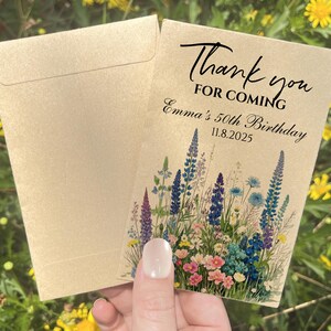 Puede incluir: Un juego de sobre y tarjeta de papel kraft. La tarjeta presenta el texto "Thank you for coming" y "Emma's 50th Birthday 11.8.2025". La tarjeta est&aacute; decorada con un dise&ntilde;o floral en tonos azules, morados, rosas y verdes.