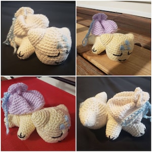 May include: Four crocheted stuffed animals in the shape of sleeping cats. The cats are in various poses and have different colored hats. The hats are purple, white, and blue.