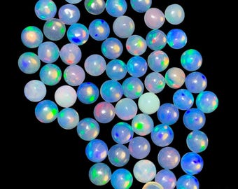 Può includere: Una collezione di gemme di opale rotonde e iridescenti. Gli opali mostrano una gamma di colori, tra cui blu, verde, giallo e rosa, con una lucentezza perlacea. Le gemme sono sparse su uno sfondo nero.