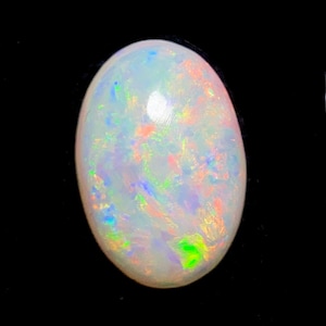 May include: An oval-shaped cabochon opal gemstone featuring a translucent white base with a vibrant play-of-color. The stone displays scattered flashes of neon green, bright orange, and soft blue light across its smooth, polished, domed surface.