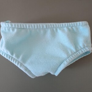 May include: Light blue underwear with elastic waistband and leg openings. The garment is made of a soft, light-colored fabric. The underwear is designed with a classic brief style.