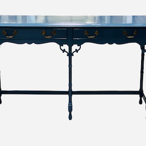 May include: A blue console table with two drawers and brass handles. The table has a scalloped edge and bamboo-style legs. The top is a lighter shade of blue. A decorative piece for a living room or entryway.