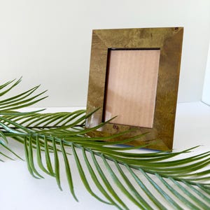 May include: A rectangular picture frame with a smooth, olive-toned wooden finish and a visible grain pattern. The frame features mitered corners and a central opening containing a plain, light brown cardboard insert for displaying a photograph.