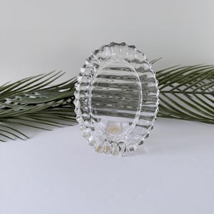 May include: Clear glass oval-shaped dish with a ruffled edge. The dish is transparent, allowing light to pass through. The design features a scalloped rim, adding a decorative element. The dish is likely used for serving or display.