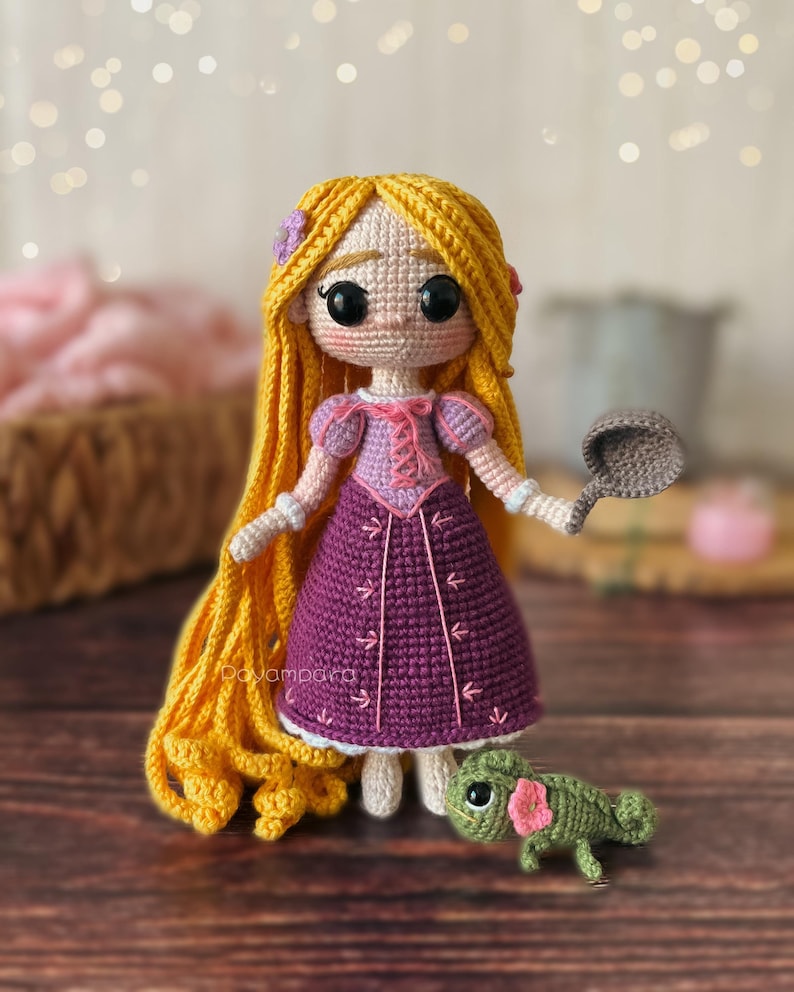 May include: A crocheted doll with long blonde hair wearing a purple dress and holding a frying pan. A green crocheted chameleon is sitting in front of the doll.