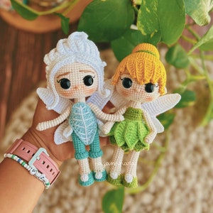 Puede incluir: Dos muñecas de hadas de crochet, una con cabello blanco y un vestido de hoja verde, la otra con cabello amarillo y una falda de hoja verde.
