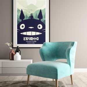 K&ouml;nnte beinhalten: A framed poster with a black frame, depicting Totoro from My Neighbor Totoro. The poster hangs above a teal armchair with wooden legs. The Japanese text is visible. The room also features a white cabinet and decorative vases.