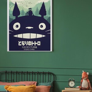 K&ouml;nnte beinhalten: Ein gerahmtes Poster mit einer dunkelblauen Silhouette von Totoro mit einer Waldszene und dem japanischen Text "となりのトトロ" und "STUDIO GHIBLI". Das Poster h&auml;ngt an einer gr&uuml;nen Wand &uuml;ber einem Bett mit bunten Kissen.