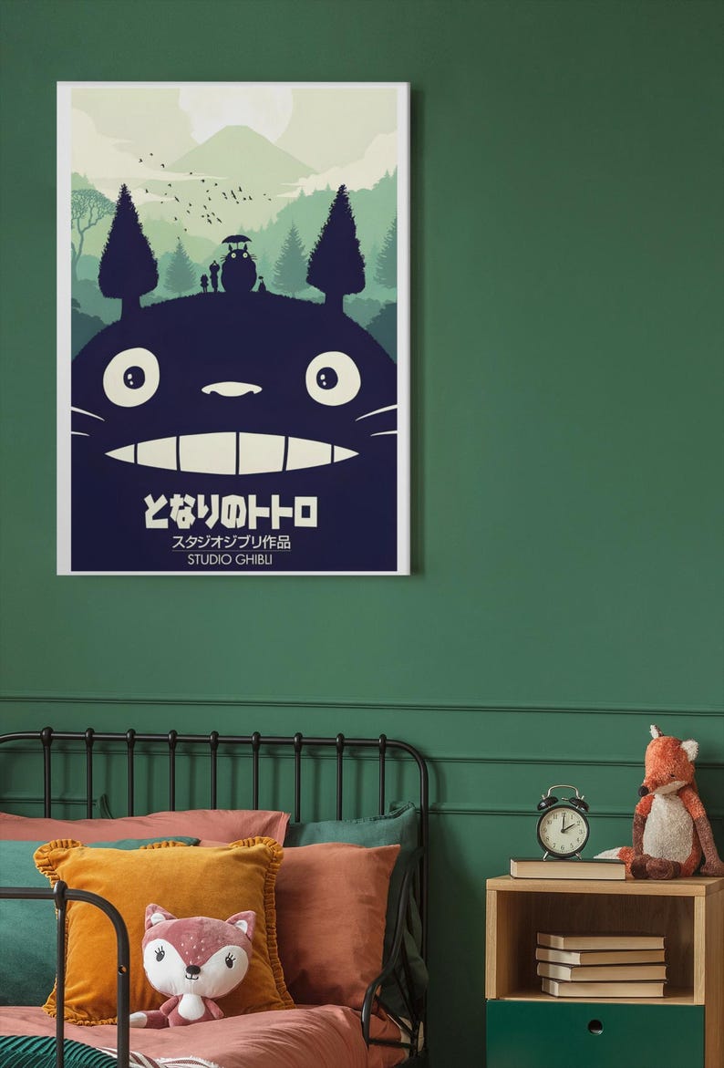 K&ouml;nnte beinhalten: Ein gerahmtes Poster mit einer dunkelblauen Silhouette von Totoro mit einer Waldszene und dem japanischen Text "となりのトトロ" und "STUDIO GHIBLI". Das Poster h&auml;ngt an einer gr&uuml;nen Wand &uuml;ber einem Bett mit bunten Kissen.