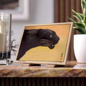 May include: A framed print depicting a black panther in profile, set against a yellow and orange backdrop. The artwork features Japanese influences, with text in the lower right and the words "Black Panther" at the bottom left.