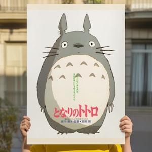 Pode incluir: Um cartaz com o personagem animado Totoro do filme "Meu Vizinho Totoro". O cartaz tem um fundo branco com uma grande figura cinza de Totoro com uma barriga creme. Texto japon&ecirc;s &eacute; vis&iacute;vel.