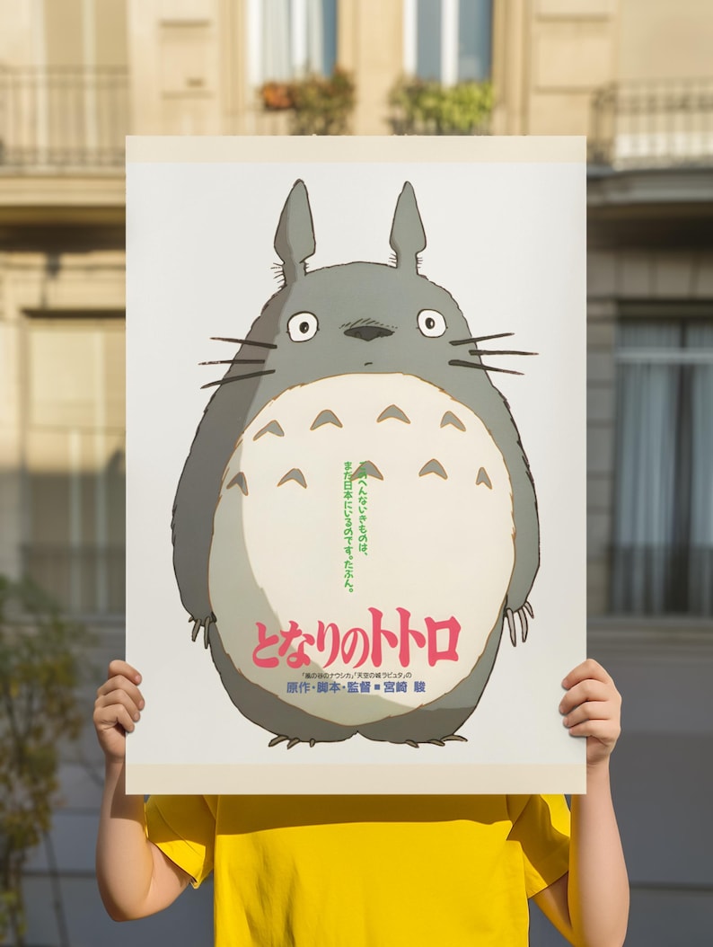 Pode incluir: Um cartaz com o personagem animado Totoro do filme "Meu Vizinho Totoro". O cartaz tem um fundo branco com uma grande figura cinza de Totoro com uma barriga creme. Texto japon&ecirc;s &eacute; vis&iacute;vel.