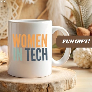 Könnte beinhalten: Weiße Keramiktasse mit dem Text "WOMEN IN TECH" in bunten Buchstaben. Die Tasse steht auf einem Untersetzer aus Holz. "FUN GIFT!" steht in brauner Schrift auf einem braunen Rechteck.