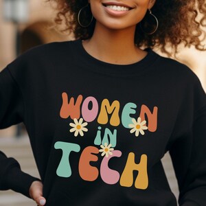 Puede incluir: Sudadera negra con el texto "Women in Tech" en letras retro de colores y detalles de flores.