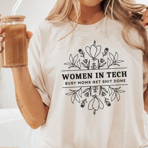 May include: White t-shirt with black text and floral design that reads "Women in Tech Busy Moms Get Shit Done"