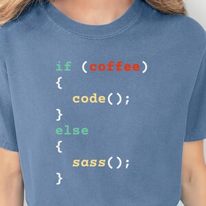May include: A blue t-shirt with the text "if (coffee) { code(); } else { sass(); }" in a programming code style. The text is in various colors, including red, green, and yellow. The shirt is a casual style.