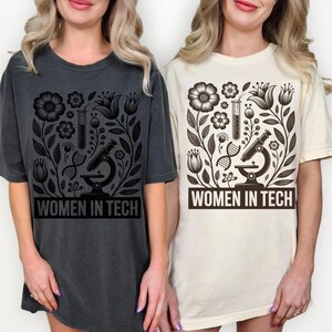 May include: Two t-shirts, one dark gray and one cream, each featuring a black floral design with a microscope, test tube, and DNA strand. The text "WOMEN IN TECH" is printed at the bottom of each shirt.