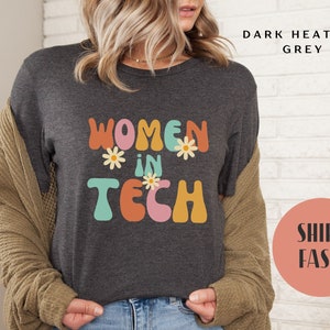 May include: Dark heather grey t-shirt with the text "Women in Tech" in colourful retro lettering and flower accents.