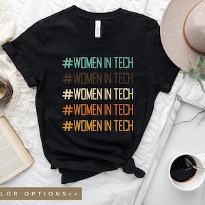 May include: Black t-shirt with the text "#WOMEN IN TECH" repeated five times in different colors, including teal, brown, orange, and yellow. The text is stacked vertically on the shirt.